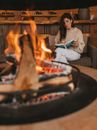 Woman Holding a Book Beside Fireplace