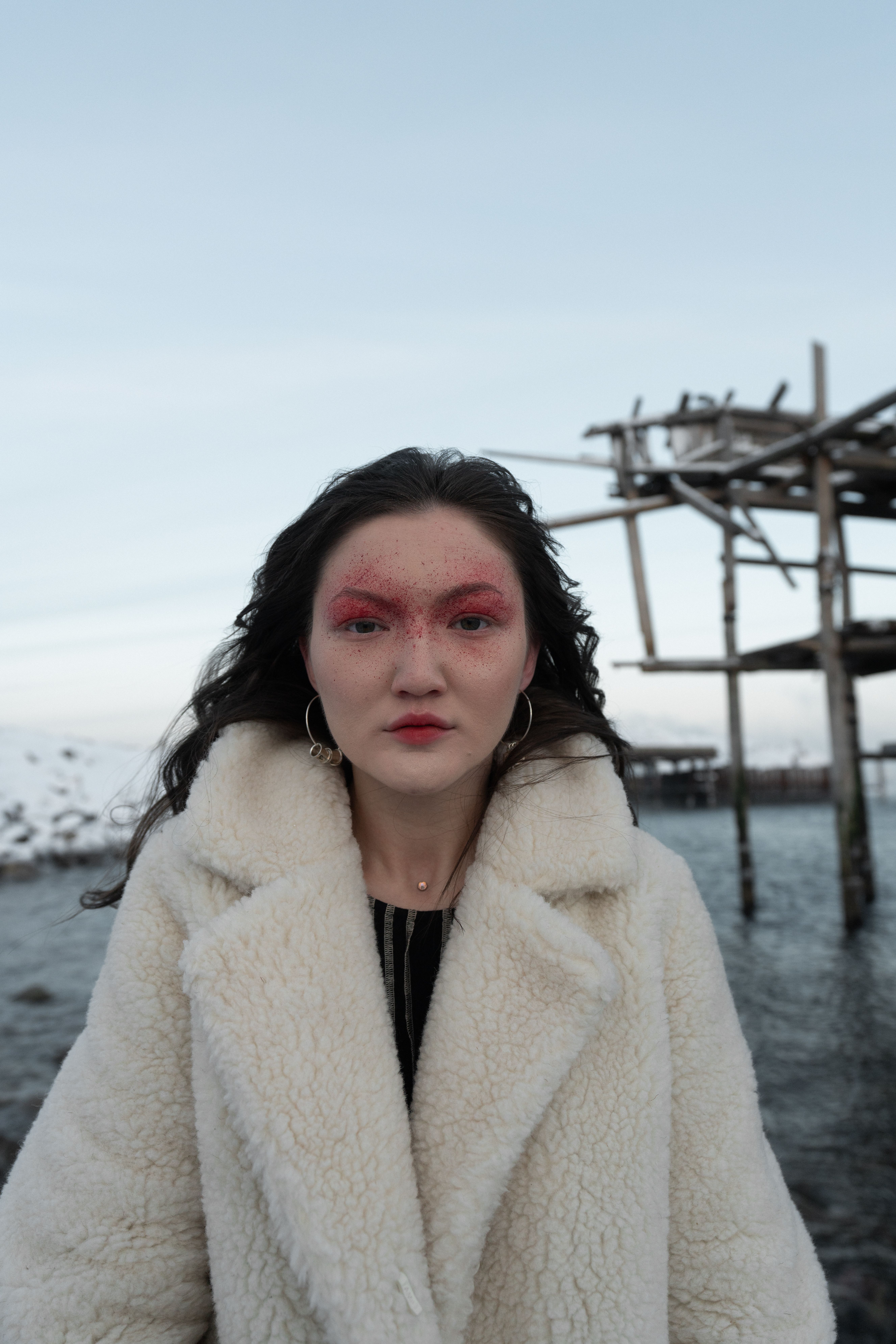 Asian woman in fur coat by the sea, embodying winter fashion.