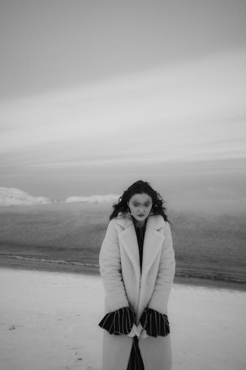 A Woman Standing on a Beach Wearing a Fur Coat