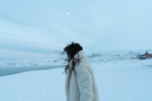 Person in White Fur Coat Standing on Snow Covered Ground