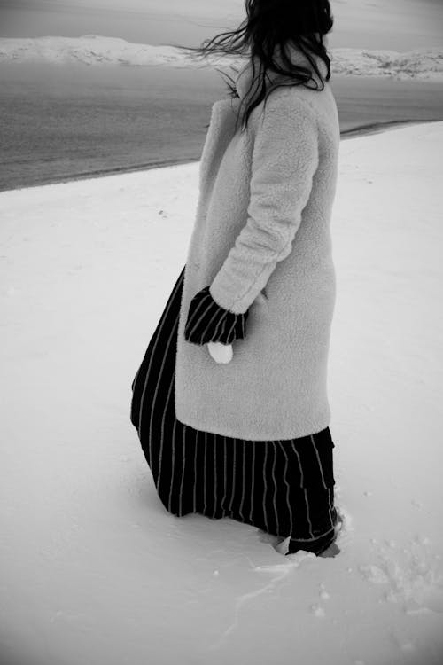 A Grayscale of a Woman Wearing a Fur Coat Walking on Snow