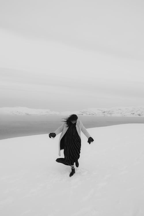 A Grayscale of a Woman Wearing a Fur Coat Walking on Snow