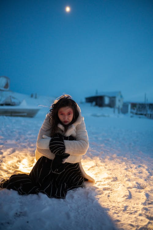 Woman Wearing Winter Coat while Sitting on Snow-Covered Ground
