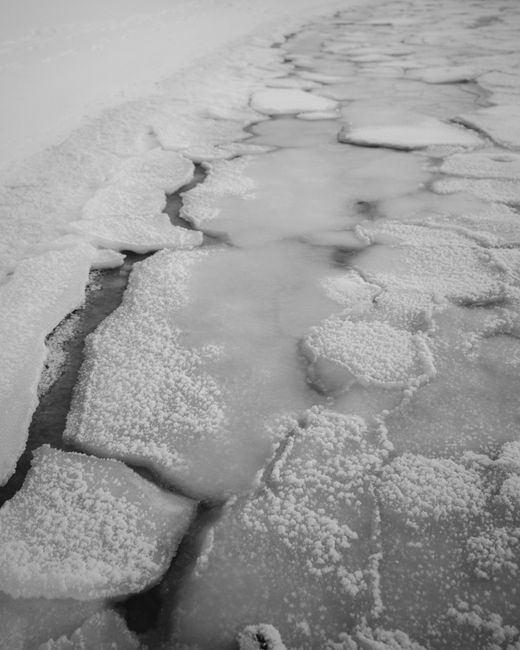 Black and white image of a frozen river with intricate cracked ice formations.