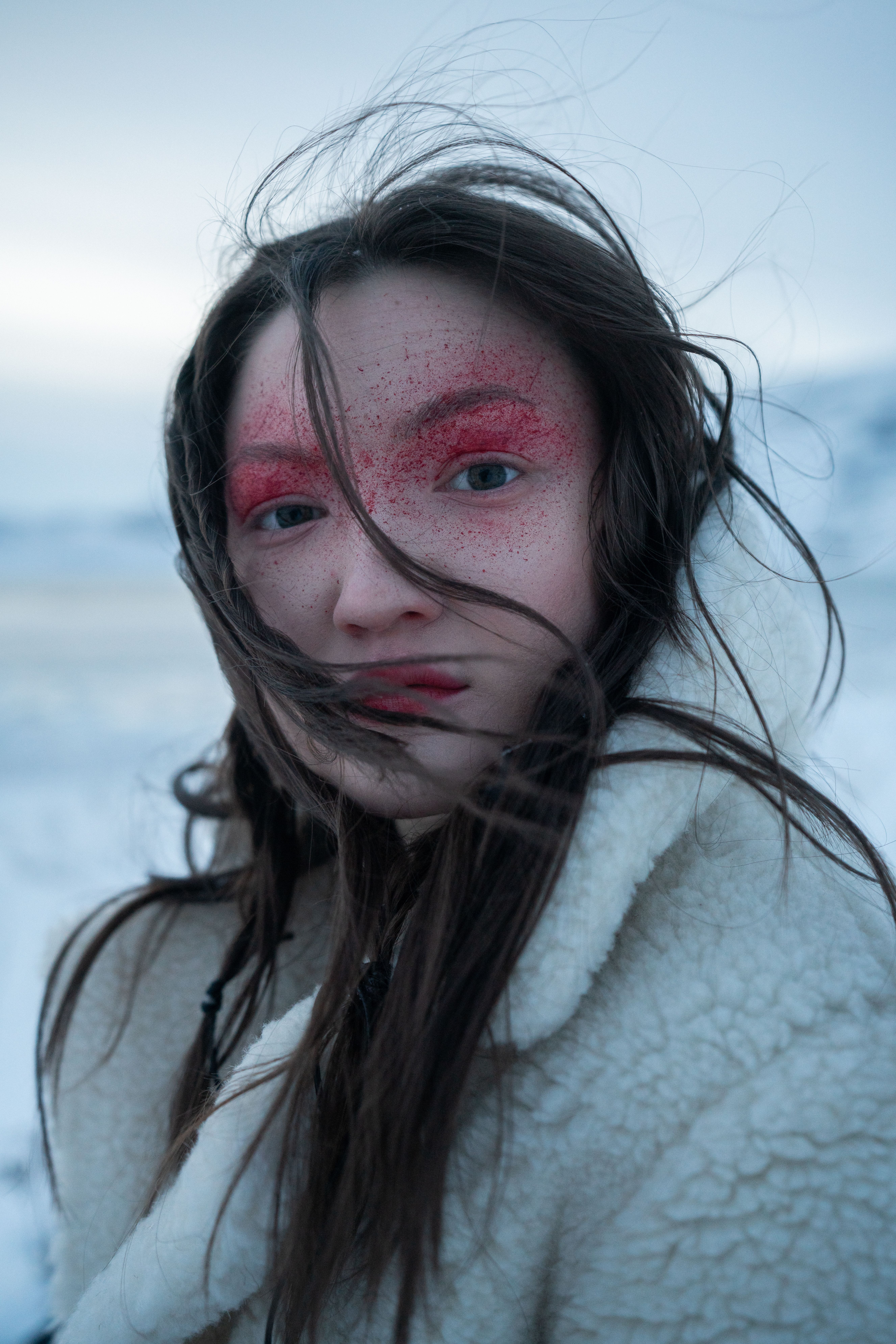 Creative winter portrait of a young woman with striking red eyeshadow in a snowy landscape.
