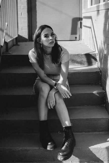 Grayscale portrait of a young woman sitting on stairs wearing black boots.