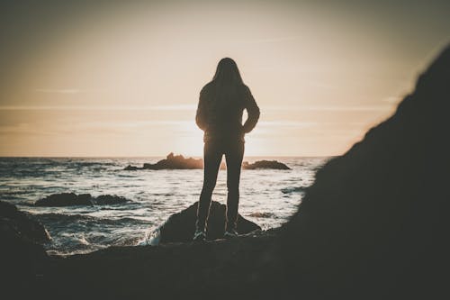 Silhouette of a Woman Standing on a Rocky Shore during Sunset