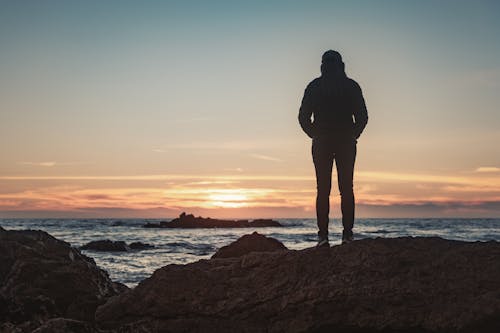 Back View Shot of a Woman Standing on a Rocky Shore during Golden Hour