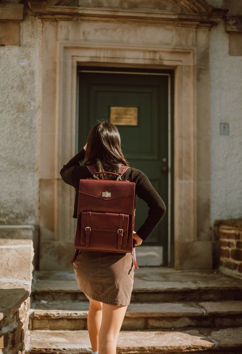 Free A woman with a leather backpack stands on stone steps, facing a wooden door. Stock Photo