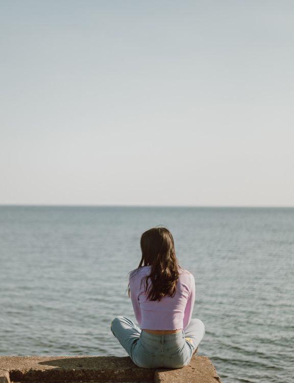 Back View of a Woman Sitting on Rock in Front of the Sea · Free Stock Photo