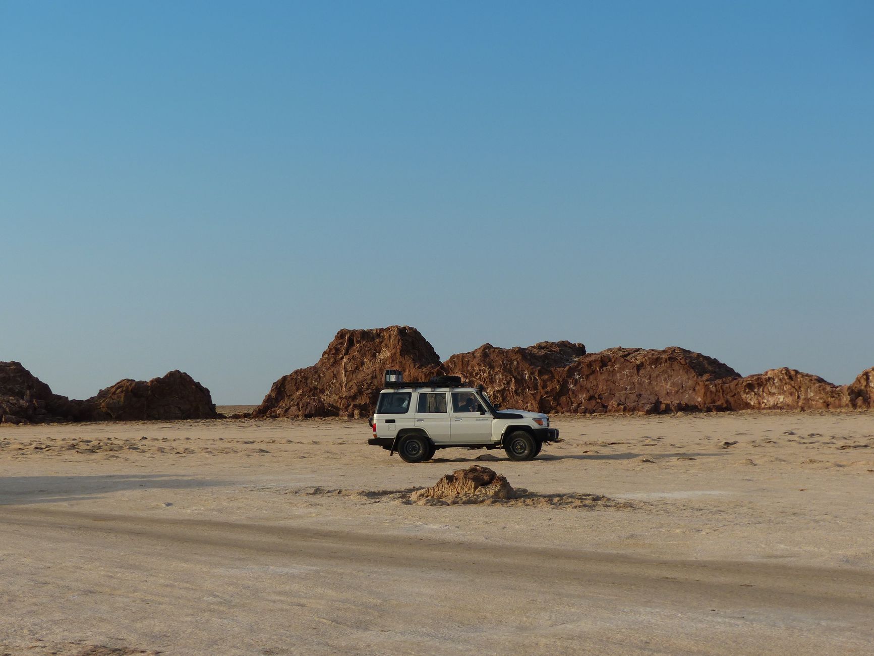 A 4x4 SUV parked in the Ethiopian desert with rocky formations under a clear blue sky.