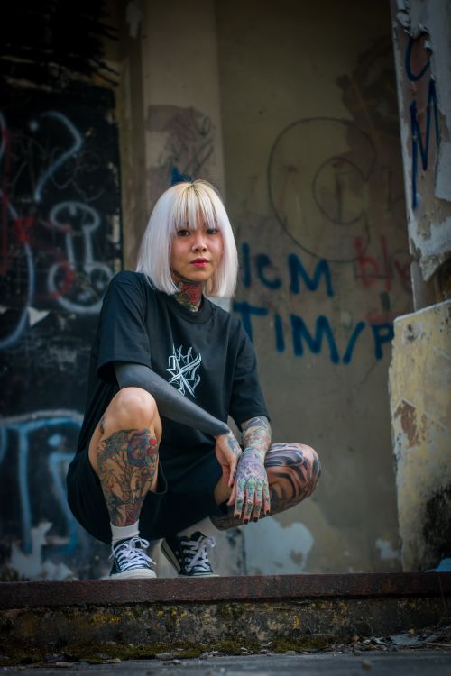 Free Blonde woman with tattoos squats in a graffiti-filled alley, showcasing street style. Stock Photo