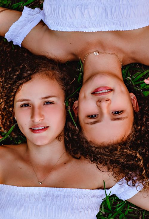Free Two young twin girls with curly hair lying on grass, embodying youth and vitality. Stock Photo