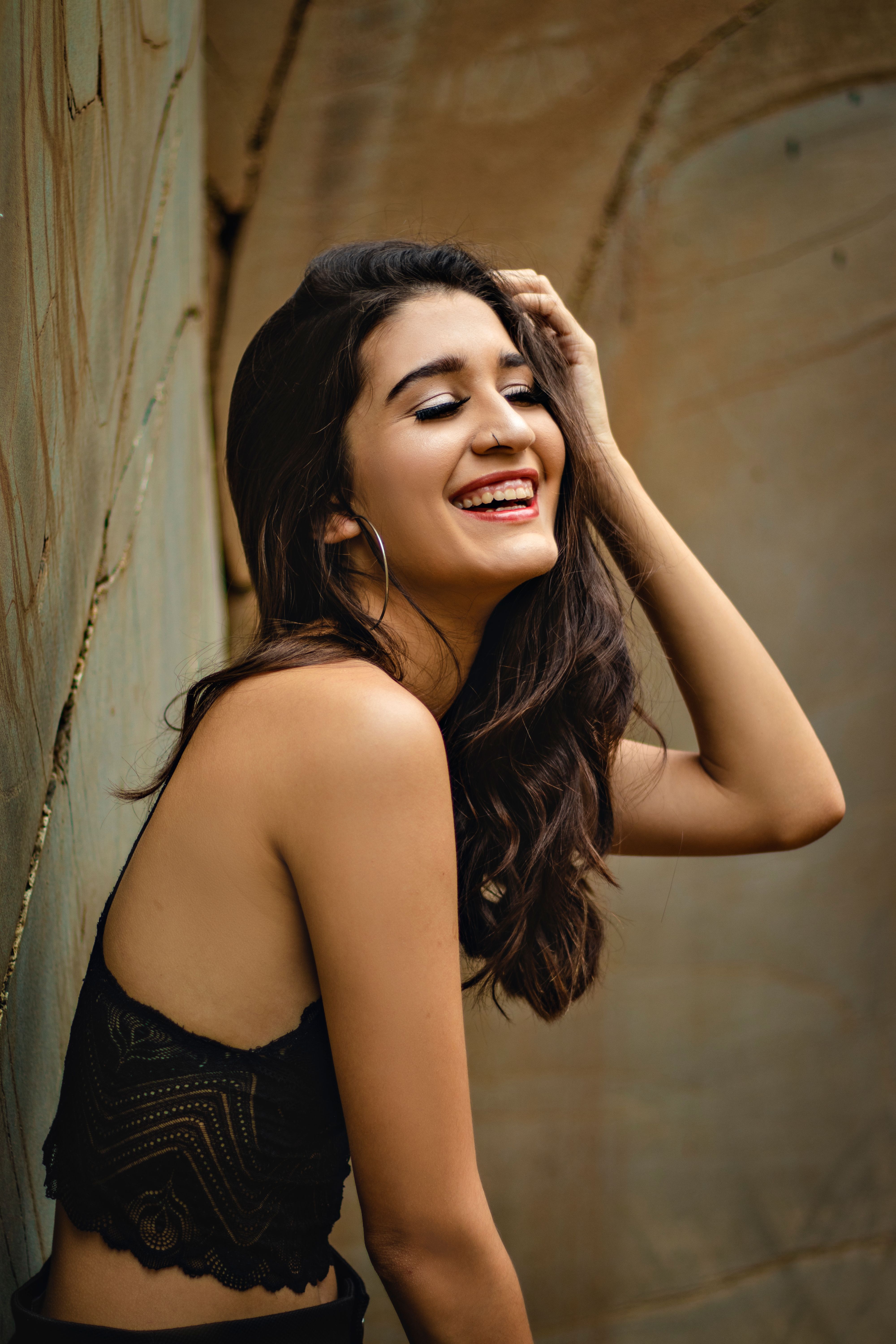 A young woman with long hair smiles joyfully against a rustic background.