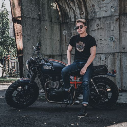 Free A stylish man in sunglasses and jeans sits on a rugged motorcycle outdoors against a concrete wall. Stock Photo