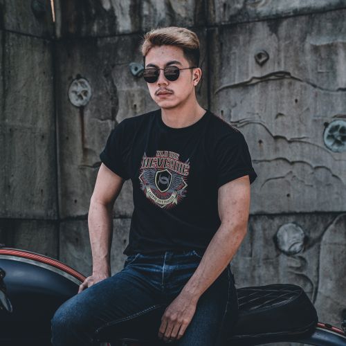Free A stylish young man in sunglasses poses confidently on a motorcycle against a textured wall. Stock Photo