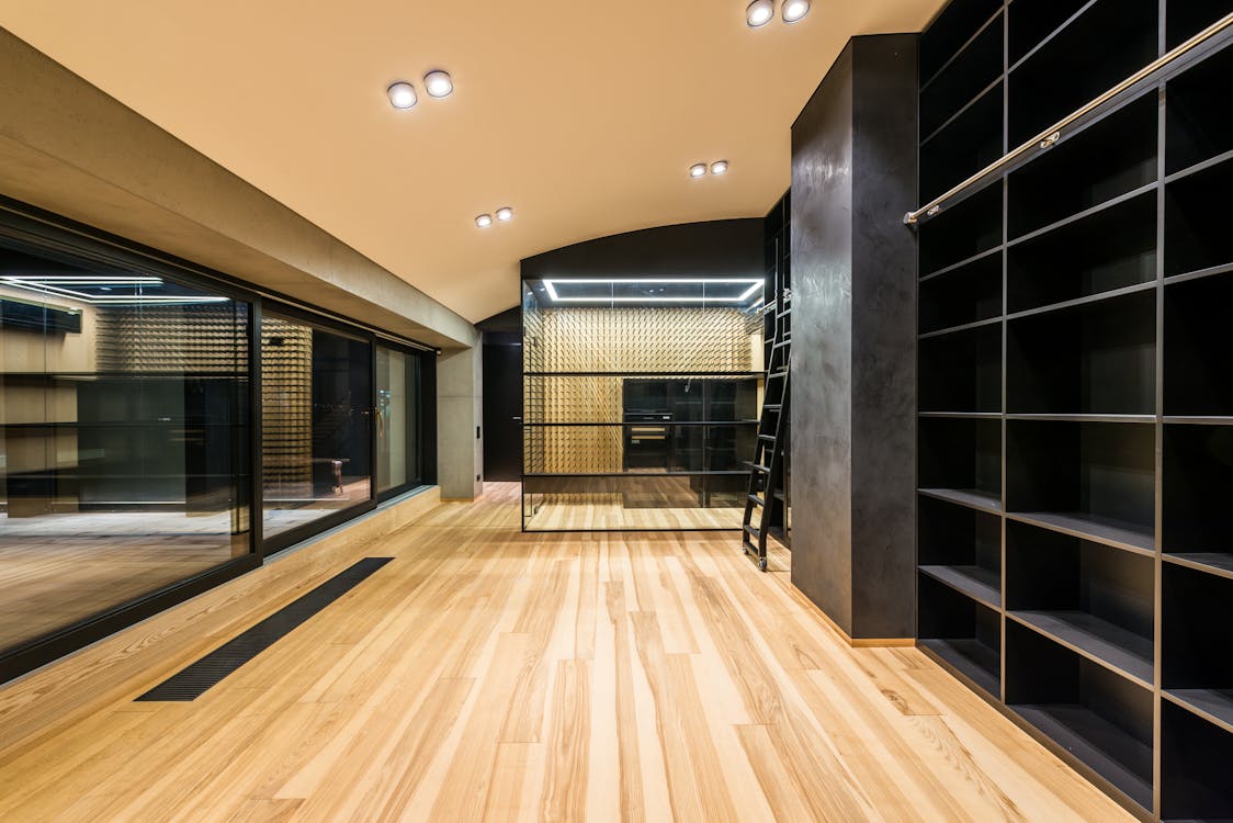Wine cellar with ladder and shelves reflecting in mirrors on parquet under lamps in building