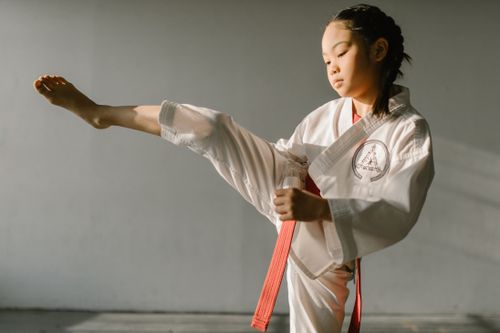 Free Focused young girl practicing taekwondo kick with red belt indoors. Stock Photo