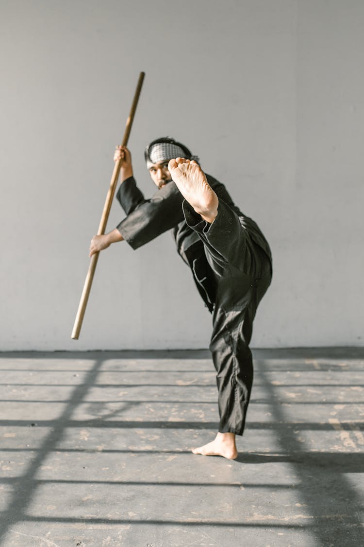 A Man In Black Gi Holding Wooden Stick