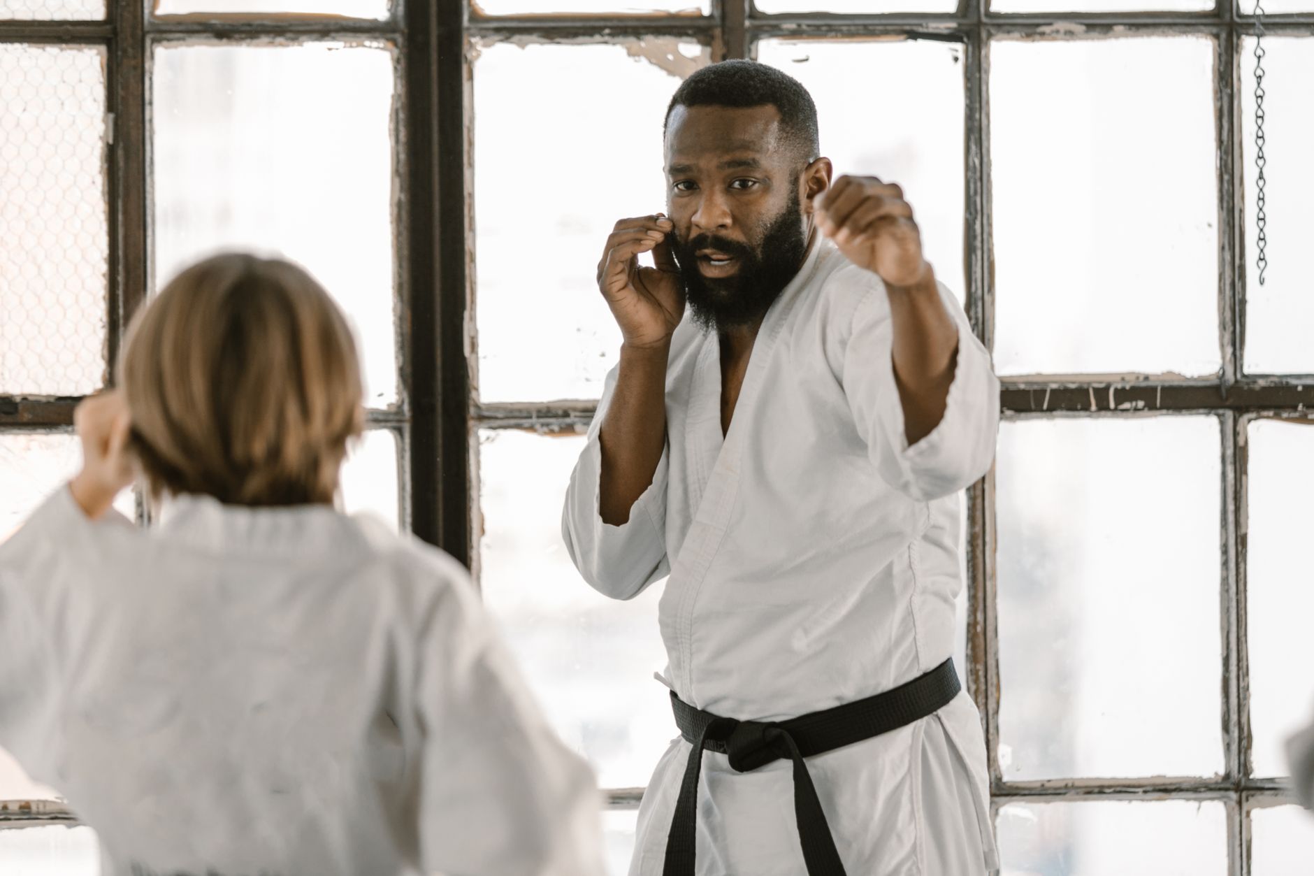 Martial arts fighters practice in a sunlit dojo, focusing on technique and discipline.