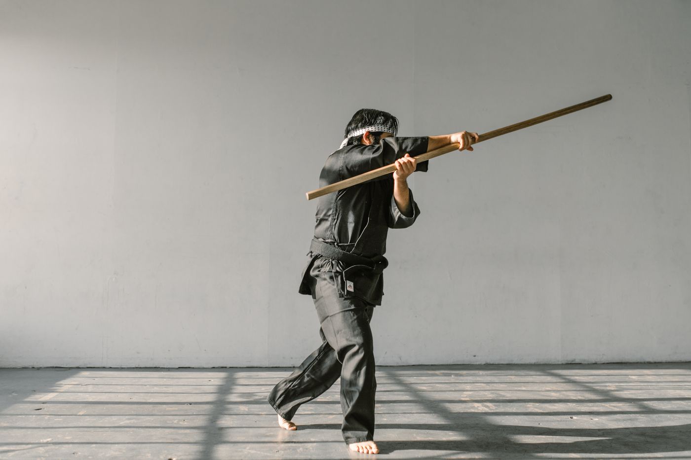 Martial artist practising with a traditional wooden staff during indoor training.