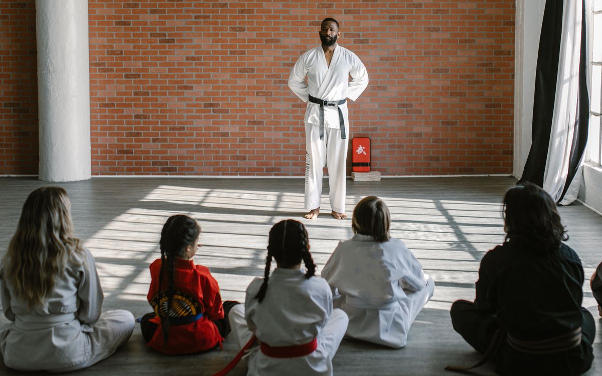 Young students in gis learn martial arts under the guidance of a black belt sensei in a dojo setting.