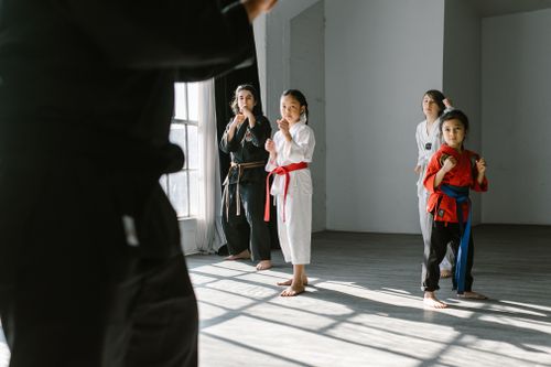 Free Group of children practicing martial arts indoors, guided by an instructor, in a sunlight-lit dojo. Stock Photo