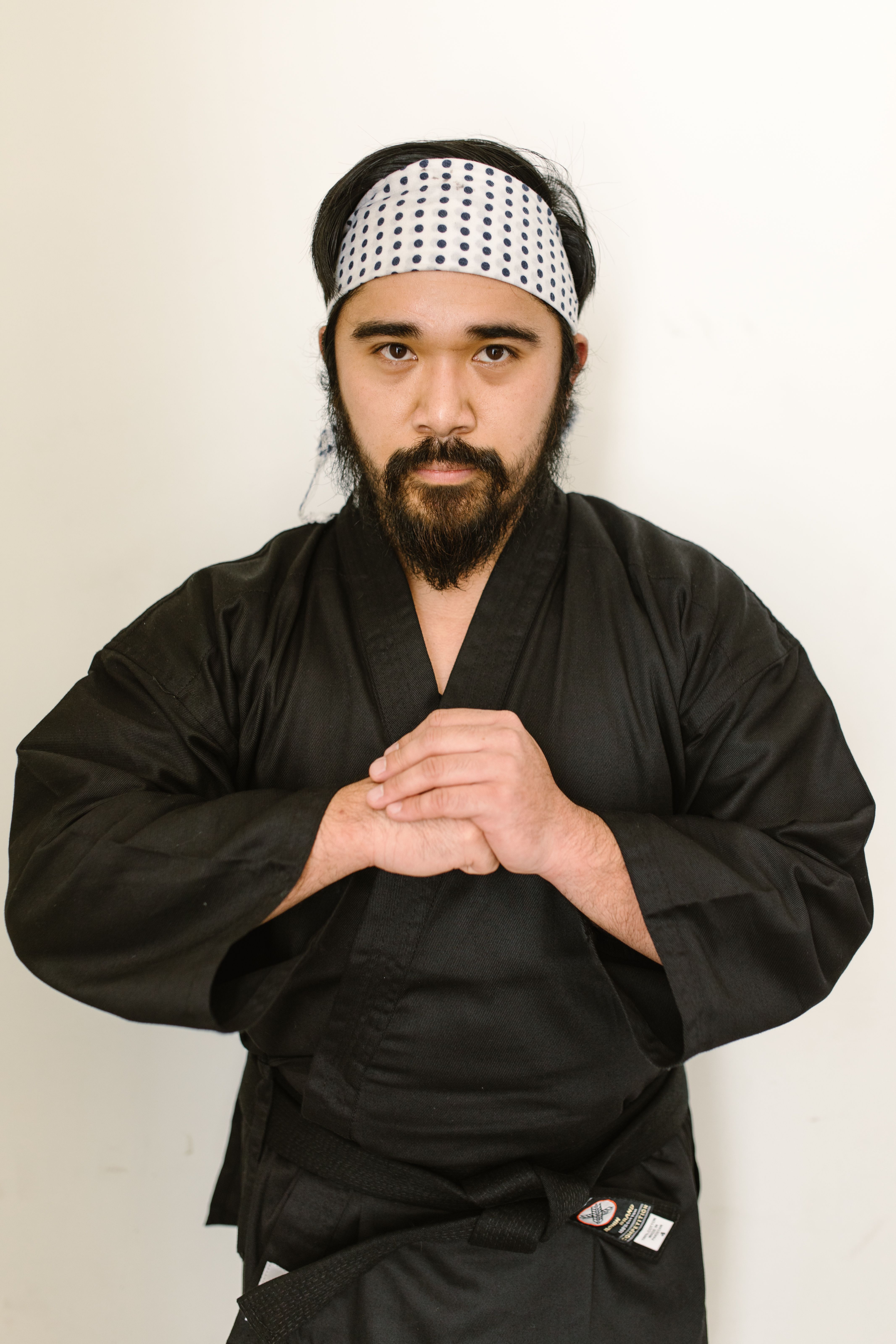Portrait of a martial artist in a karate pose wearing a black uniform and bandana.