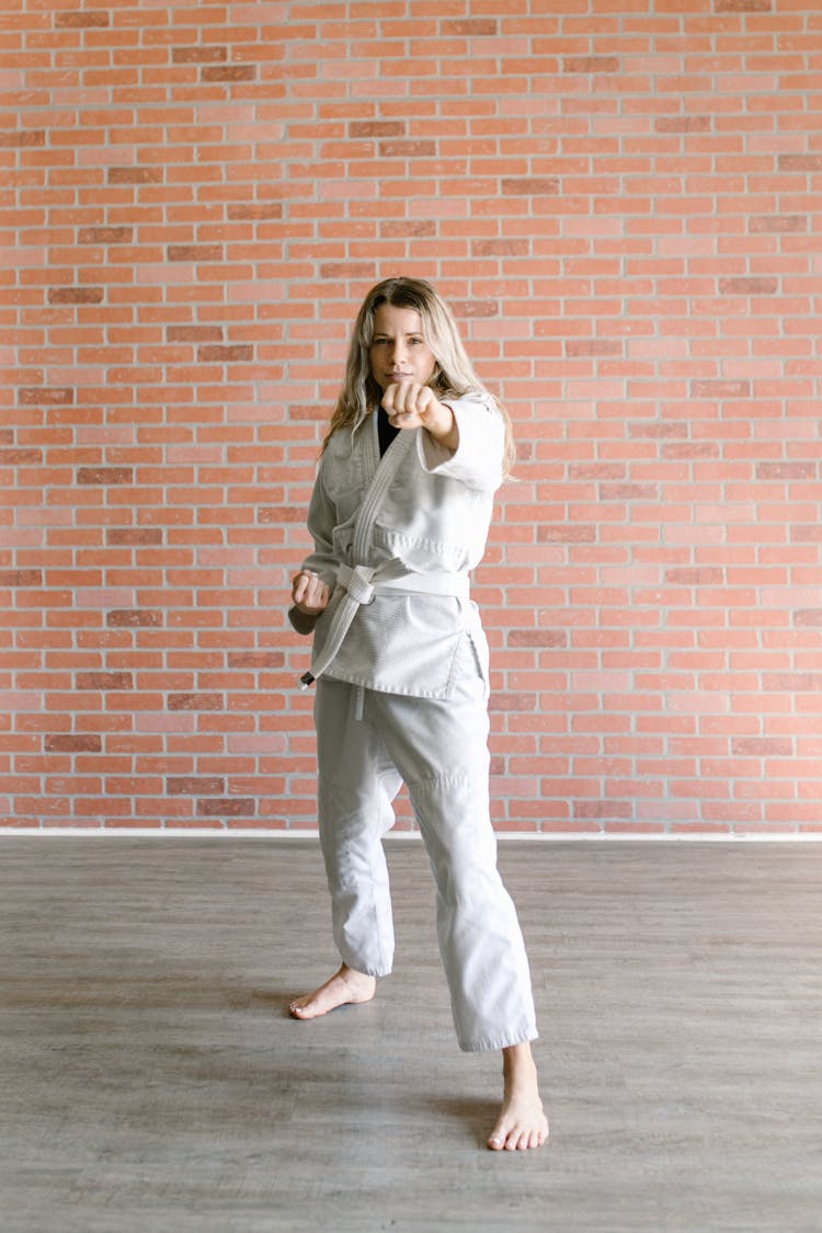 A Woman In Taekwondo Uniform While Standing Near The Brick Wall