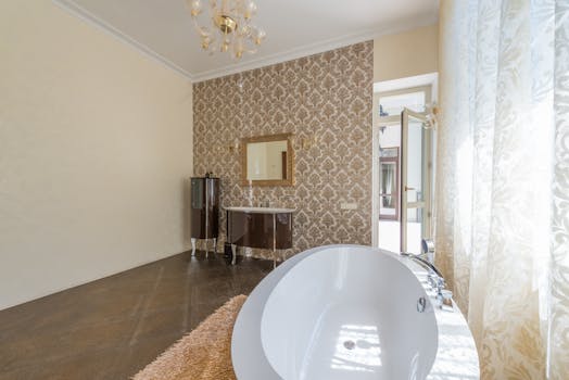 Spacious luxury bathroom with a stylish chandelier and ornate wallpaper.
