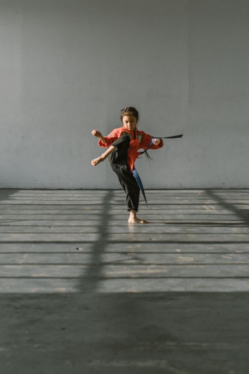 Free Young girl practicing a high kick in martial arts studio with determination. Stock Photo