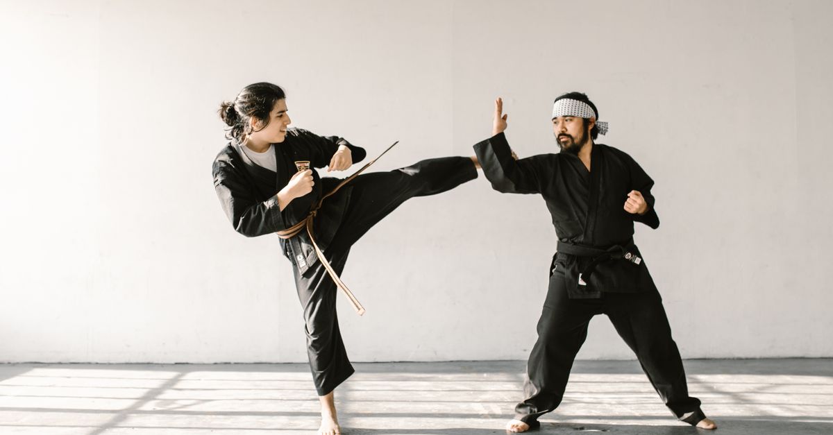 Two adult martial artists wearing black uniforms practicing an advanced kicking and blocking technique, illustrative of a beginner karate training guide concept.