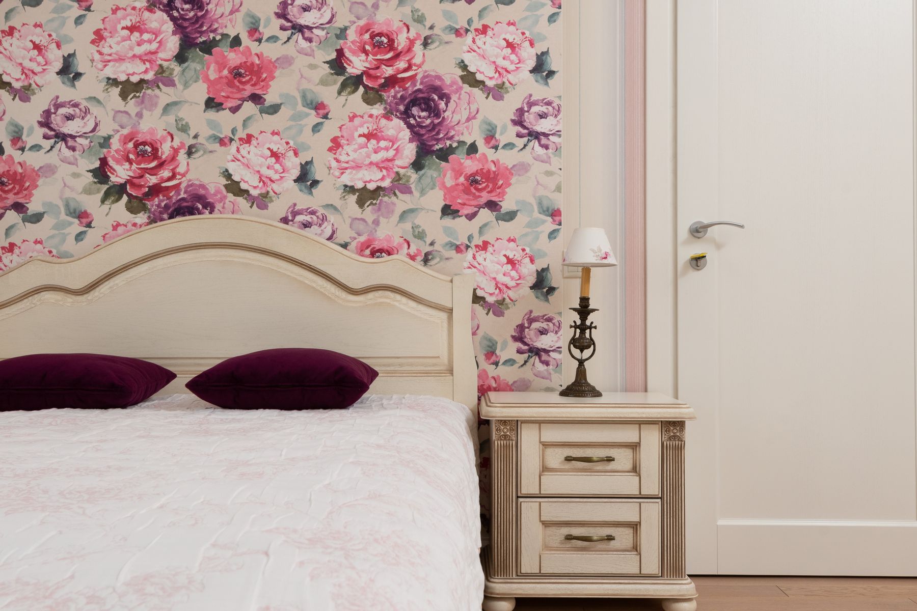 Bed with pale layered bedding, blue floral wall and warm wood nightstand