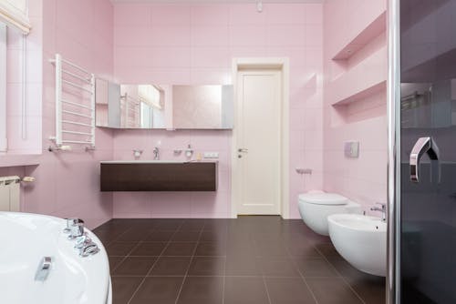 Interior of modern bathroom in pink and brown colors with white bathtub and glass shower cabin and mirror hanging on wall