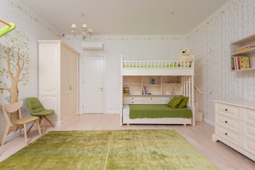 Interior of cozy light bedroom for kid with double deck bed and wooden shelves with decorations and green carpet