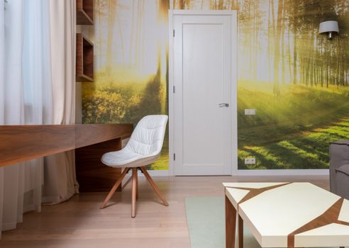 Modern light room with comfortable sofa and armchair at wooden table against colorful image of woods on wall