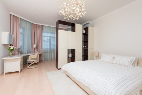 Contemporary interior of light spacious bedroom with bed and wardrobe with shelves and workplace