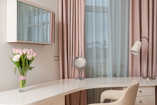 Free White table with lamp and chair under shelf with mirror near window decorated with pink curtains Stock Photo
