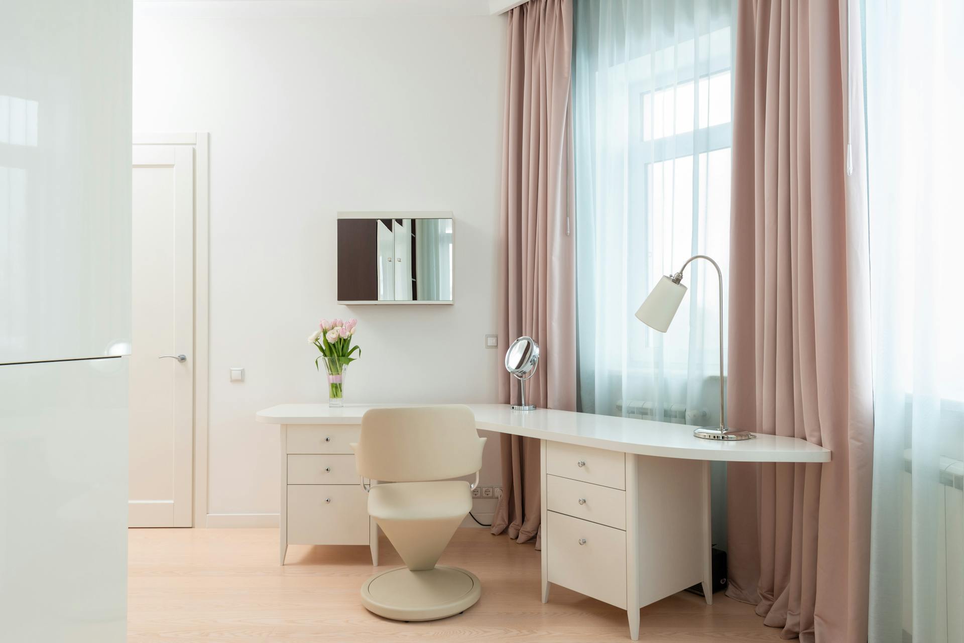 Elegant home office with minimalist design featuring white furniture, soft curtains, and natural light.