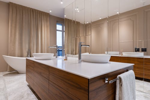 Minimalistic interior of modern bathroom with white sink and bath and mirrored cabinet in apartment in daytime