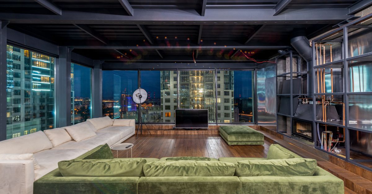 Interior of contemporary spacious living room with large comfortable sofas and panoramic windows in evening time