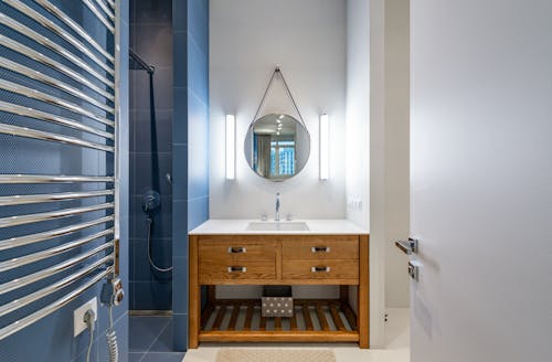 Clean sink with placed under round mirror near shower with blue tile in bathroom in modern apartment