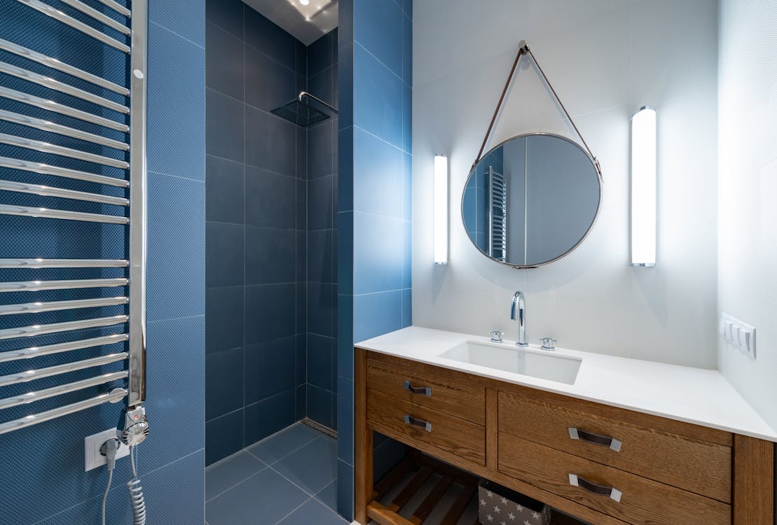 Interior of stylish bathroom with blue tile in shower and round mirror hanging on wall above sink