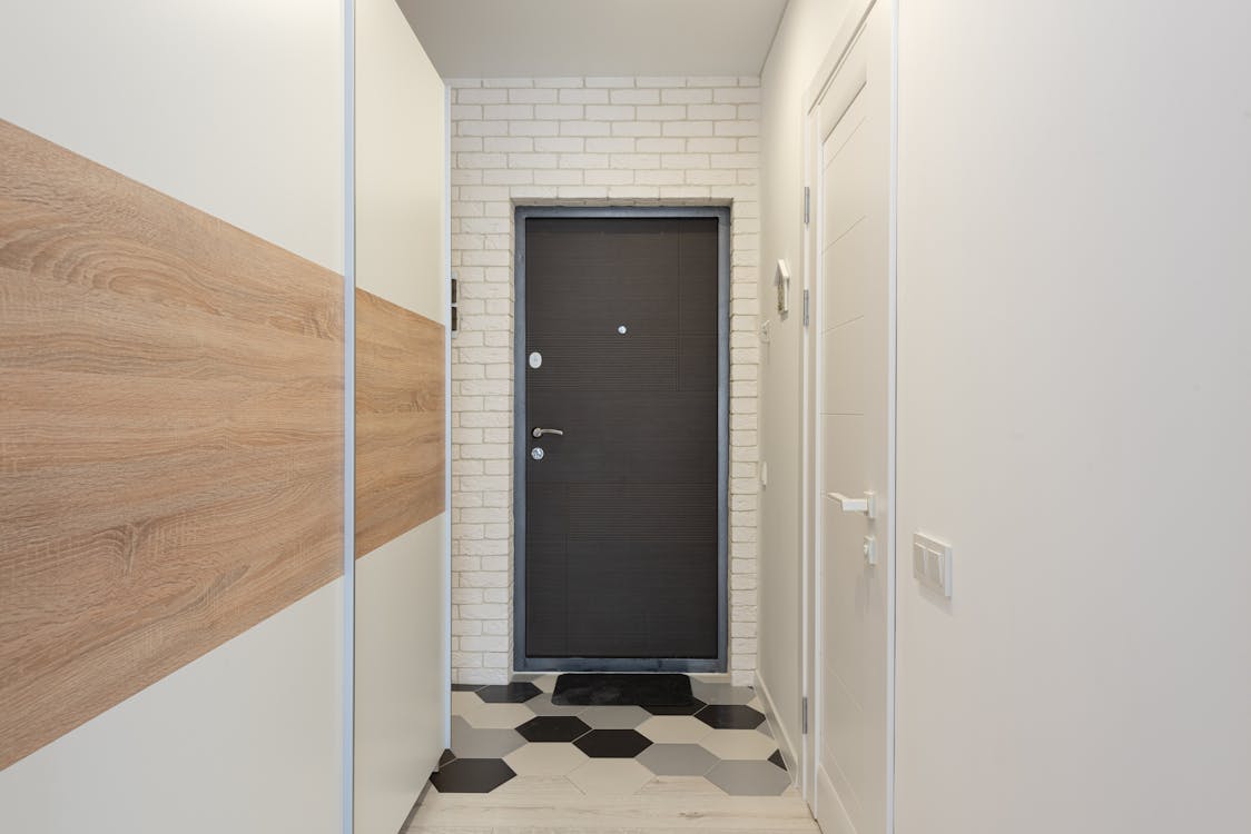 Entrance door between white brick wall against narrow passage with closet and rug with hexagonal ornament in house
