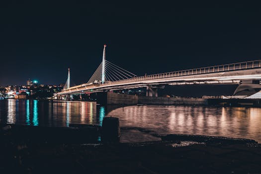 夜晚，平静的河面上，现代吊桥亮起灯光，倒映着城市的灯火