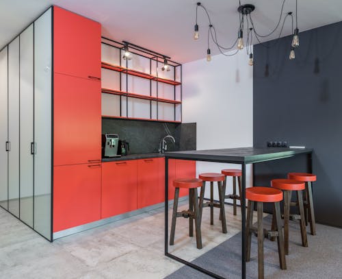 Modern kitchen interior with rows of stools under chandelier with light bulbs against refrigerator and shelves in house