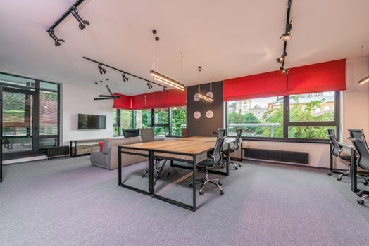 Contemporary workspace interior with armchairs and tables against TV and sofa under lamps hanging on ceiling