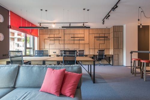 Sofa with cushions against tables and armchairs under hanging lamps in contemporary office in daylight