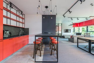 Creative design of kitchen with cabinets and shelves against tables and stools in light workspace