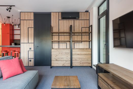 Contemporary room and kitchen interior with door against sofa and tables under television with black screen in house